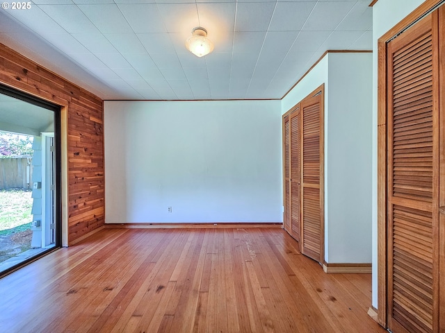 unfurnished bedroom with crown molding, baseboards, light wood-type flooring, and wood walls
