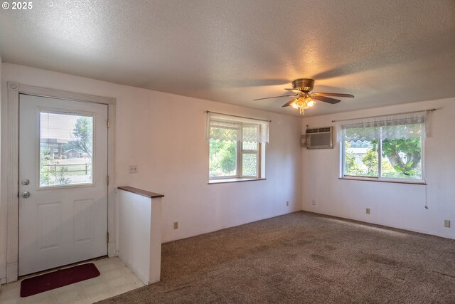 foyer entrance with a textured ceiling, a wall unit AC, ceiling fan, and light colored carpet