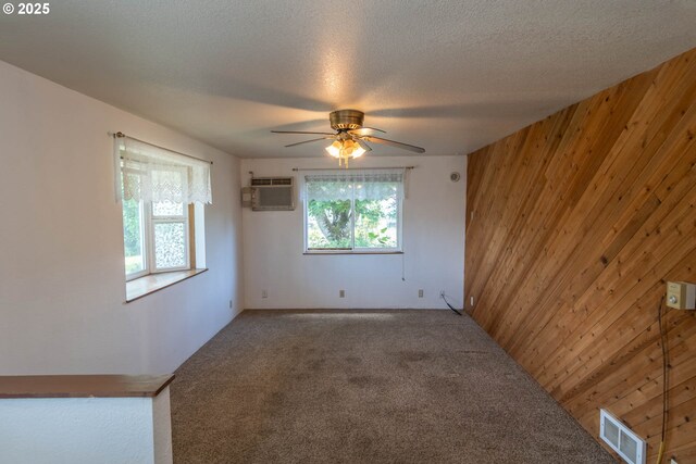 carpeted empty room featuring wood walls, a ceiling fan, a wall unit AC, and a textured ceiling