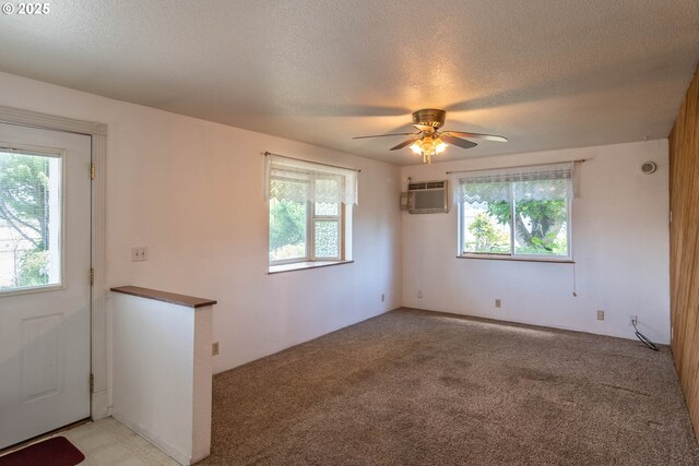 unfurnished room with healthy amount of natural light, a textured ceiling, ceiling fan, light colored carpet, and a wall mounted air conditioner