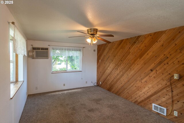carpeted empty room with wooden walls, a wall unit AC, and ceiling fan