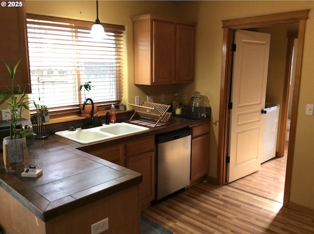 kitchen with sink, decorative light fixtures, light hardwood / wood-style flooring, stainless steel dishwasher, and tile counters