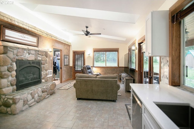 living room with lofted ceiling, a stone fireplace, and a ceiling fan