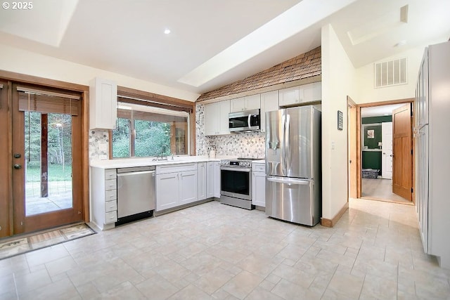 kitchen featuring a sink, stainless steel appliances, visible vents, vaulted ceiling, and backsplash