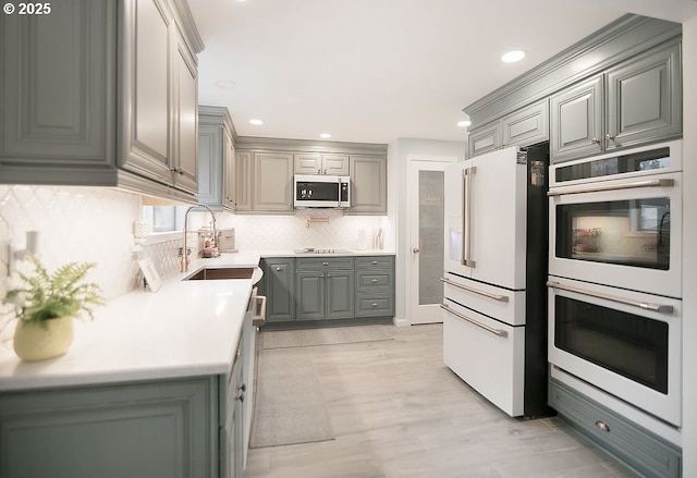 kitchen featuring gray cabinetry, white appliances, a sink, backsplash, and light countertops