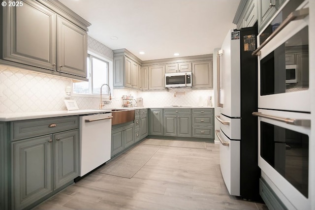 kitchen featuring gray cabinetry, white appliances, decorative backsplash, and light countertops