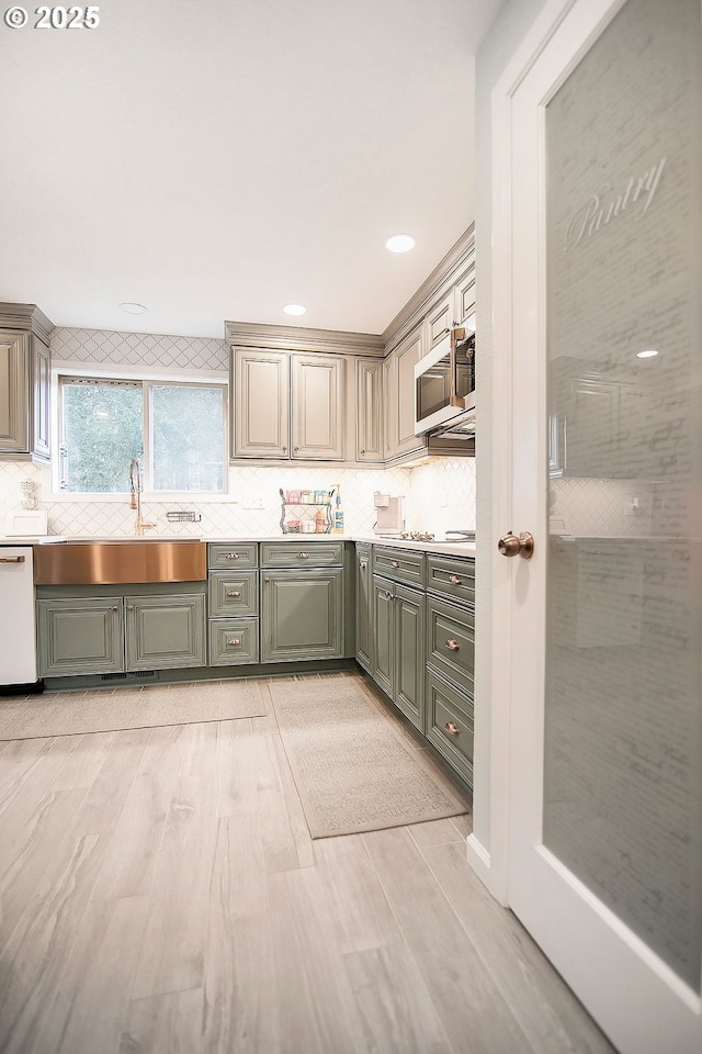 kitchen with a sink, stainless steel microwave, backsplash, white dishwasher, and green cabinets