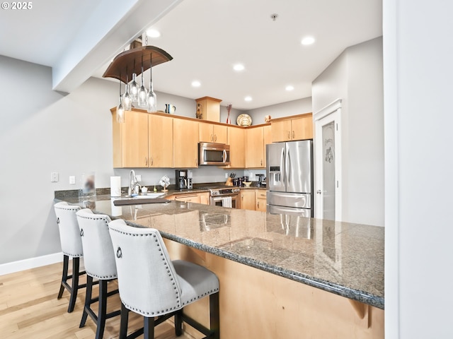 kitchen with sink, appliances with stainless steel finishes, dark stone countertops, kitchen peninsula, and light brown cabinets