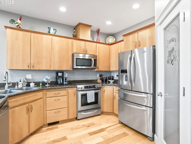 kitchen with sink, dark stone countertops, stainless steel appliances, light brown cabinets, and light hardwood / wood-style flooring