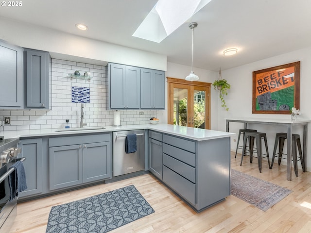 kitchen featuring a peninsula, a sink, stainless steel appliances, a skylight, and tasteful backsplash