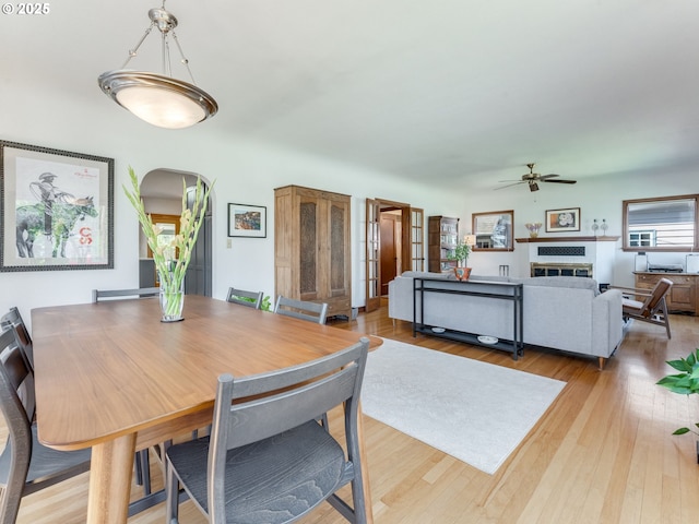 dining area with ceiling fan, light wood-style flooring, arched walkways, and a glass covered fireplace