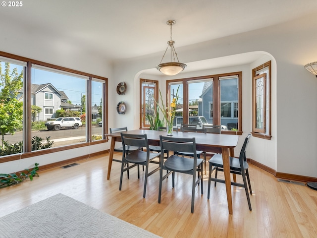 dining space featuring light wood-style flooring, arched walkways, baseboards, and visible vents