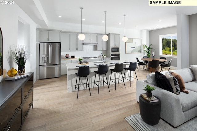 kitchen featuring appliances with stainless steel finishes, pendant lighting, an island with sink, decorative backsplash, and light hardwood / wood-style floors