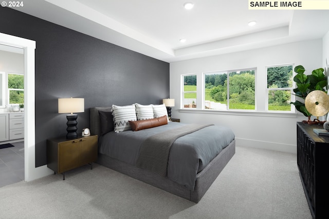 bedroom with light colored carpet, a raised ceiling, and ensuite bath