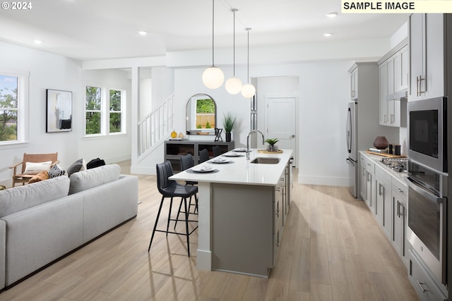 kitchen with pendant lighting, gray cabinets, stainless steel appliances, an island with sink, and a kitchen bar