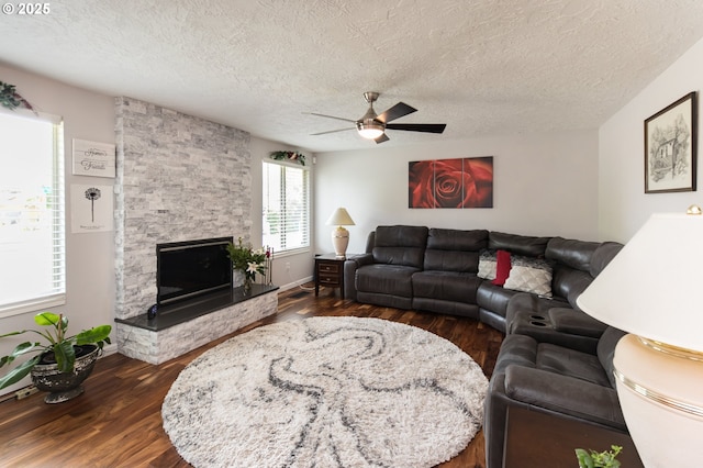 2416 SW 23rd Cir, Troutdale, OR 97060 - living room with a ceiling fan, dark wood-style floors, a stone fireplace, a textured ceiling, and baseboards