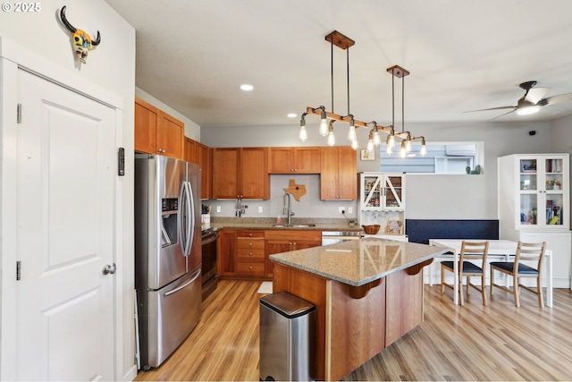 kitchen with light stone counters, stainless steel appliances, a sink, light wood finished floors, and brown cabinetry