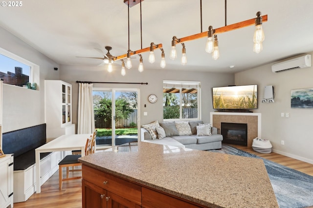 kitchen featuring light wood-style flooring, light stone counters, open floor plan, a fireplace, and a wall mounted AC