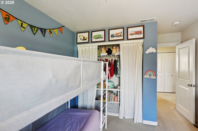 carpeted bedroom with baseboards, a textured ceiling, visible vents, and a closet