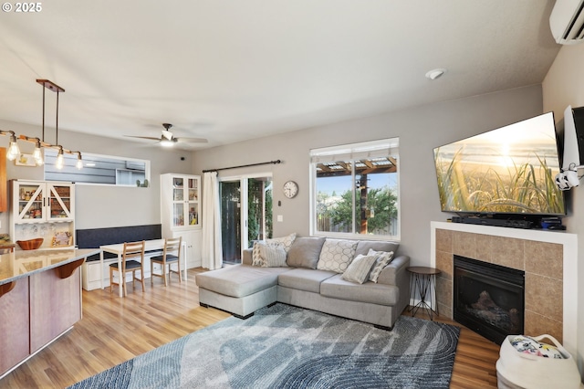 living room with light wood-style floors, a ceiling fan, a tiled fireplace, and a wall mounted AC