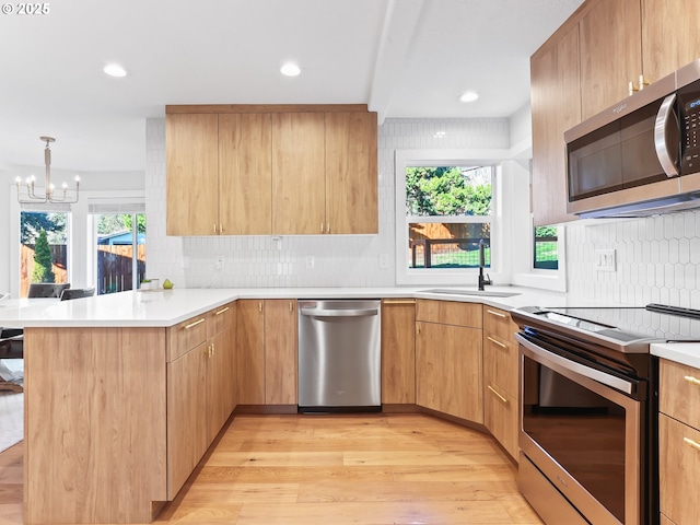 kitchen with stainless steel appliances, a peninsula, a sink, a wealth of natural light, and light wood finished floors