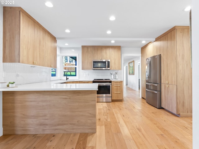 kitchen with light wood finished floors, decorative backsplash, a peninsula, stainless steel appliances, and light countertops