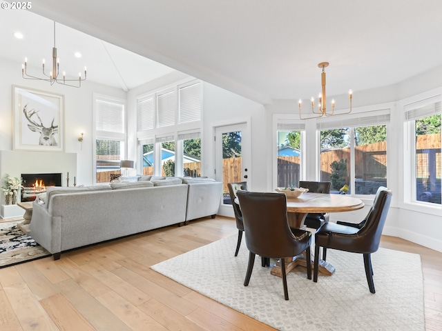 dining area featuring a warm lit fireplace, light wood-type flooring, baseboards, and an inviting chandelier