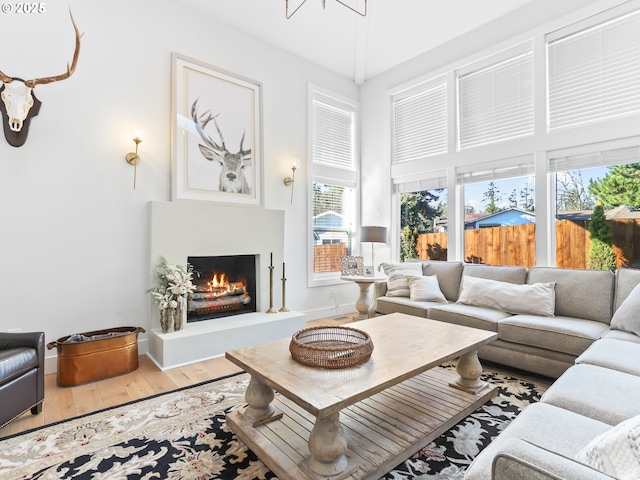 living area with a warm lit fireplace, baseboards, and wood finished floors