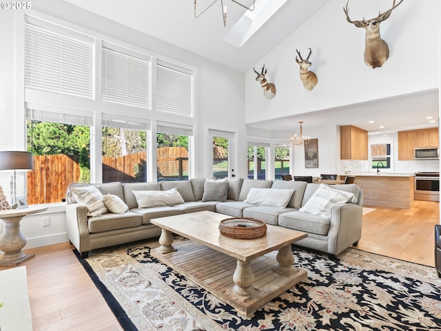 living room with a skylight, a notable chandelier, high vaulted ceiling, light wood-type flooring, and baseboards