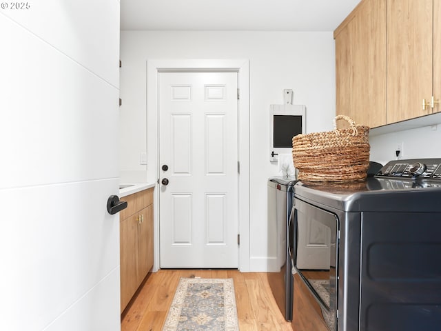 laundry area with cabinet space, light wood finished floors, and washing machine and clothes dryer