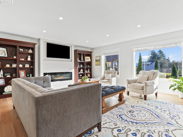 living room featuring a glass covered fireplace, light wood-style flooring, and recessed lighting