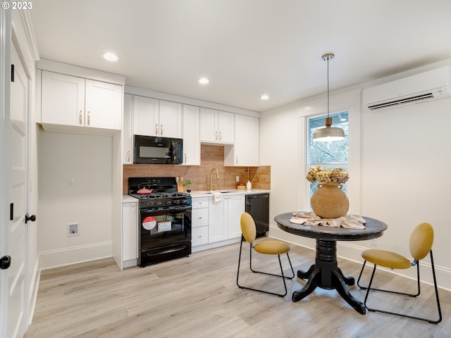 kitchen with a wall mounted air conditioner, sink, black appliances, decorative light fixtures, and white cabinetry