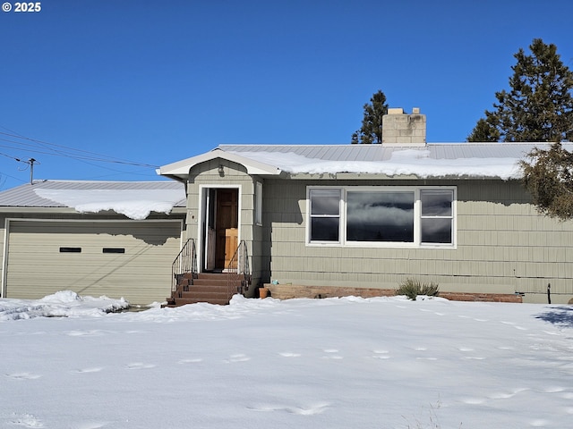 view of front of property featuring a garage, entry steps, metal roof, and a chimney