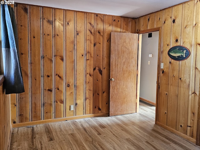 spare room with light wood finished floors, wood walls, and baseboards