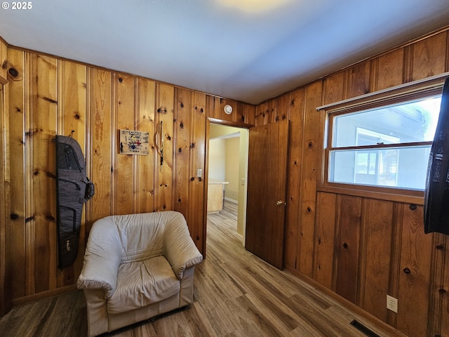 sitting room with light wood-type flooring, visible vents, and wood walls