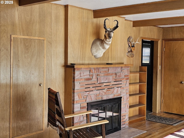 room details featuring wooden walls, beam ceiling, a stone fireplace, and wood finished floors