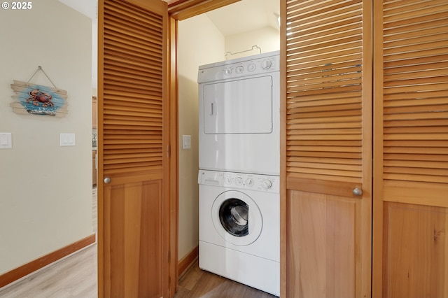 clothes washing area with stacked washer / drying machine, laundry area, baseboards, and wood finished floors