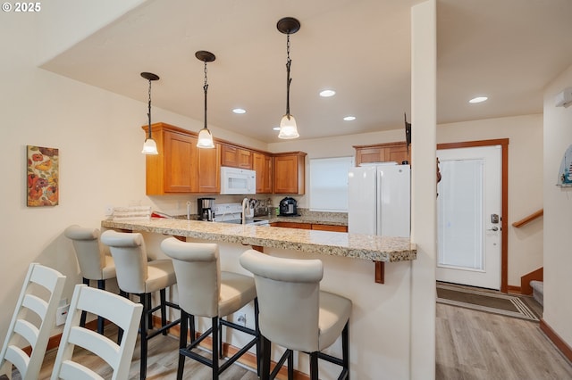 kitchen with white appliances, a peninsula, light countertops, light wood-style floors, and pendant lighting