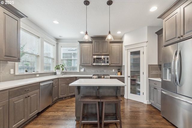 kitchen with a sink, dark wood-style floors, a center island, stainless steel appliances, and light countertops