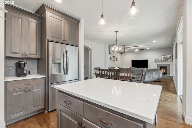 kitchen with dark wood finished floors, a lit fireplace, stainless steel fridge, open floor plan, and a center island