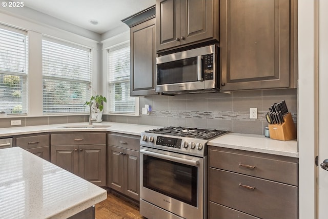 kitchen with dark wood-style flooring, a sink, stainless steel appliances, dark brown cabinets, and backsplash