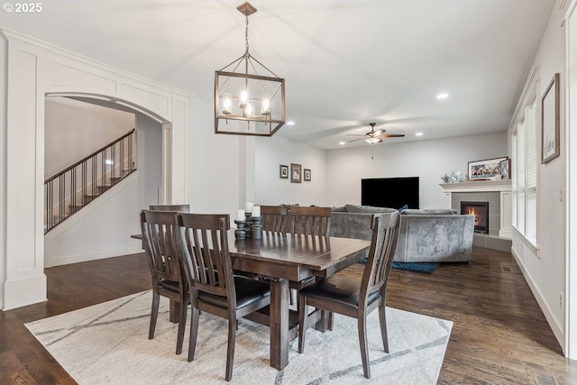 dining space featuring stairway, dark wood-style floors, a fireplace, recessed lighting, and arched walkways