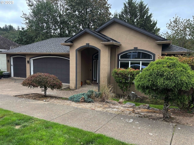 single story home featuring a garage, a shingled roof, concrete driveway, and stucco siding