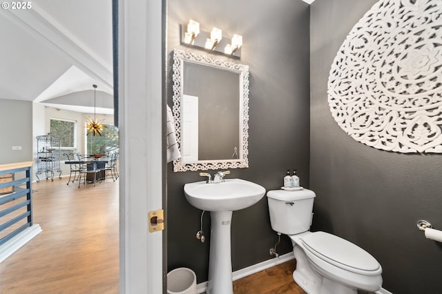 half bathroom with baseboards, wood finished floors, toilet, and a sink