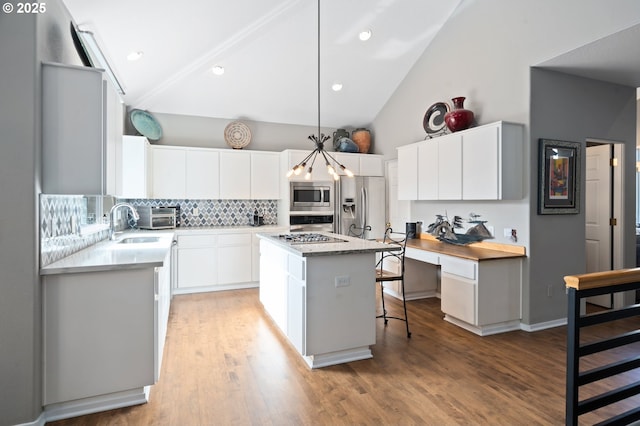 kitchen with decorative backsplash, appliances with stainless steel finishes, light countertops, a kitchen island, and a kitchen breakfast bar