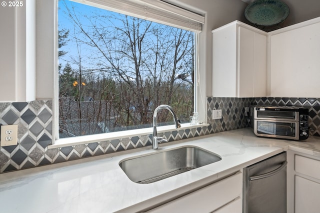 kitchen with a sink, decorative backsplash, a toaster, white cabinetry, and stainless steel dishwasher