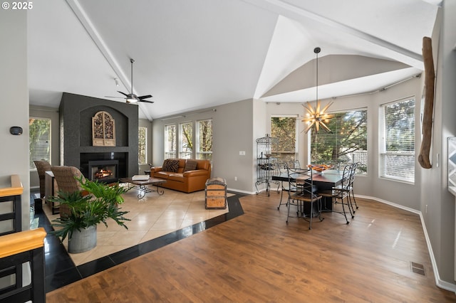 dining room featuring ceiling fan with notable chandelier, a fireplace, baseboards, visible vents, and lofted ceiling