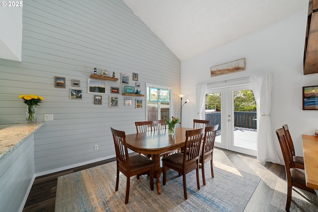 dining area featuring french doors, high vaulted ceiling, baseboards, wooden walls, and dark wood-type flooring