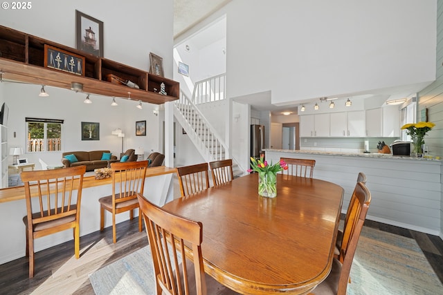 dining space featuring track lighting, a towering ceiling, dark wood-type flooring, and stairway