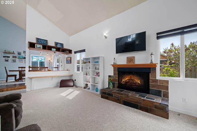 carpeted living room with a healthy amount of sunlight, high vaulted ceiling, baseboards, and a lit fireplace
